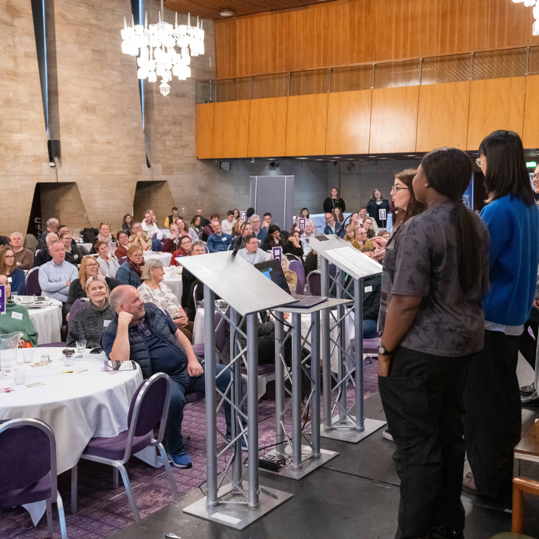 Photograph of a group of young people giving a talk to a room of conference attendees