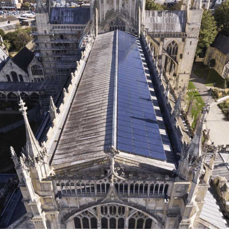 Alt text: An aerial photo looking down along the roof on a historic church. One side of the roof is covered by an array of solar panels.