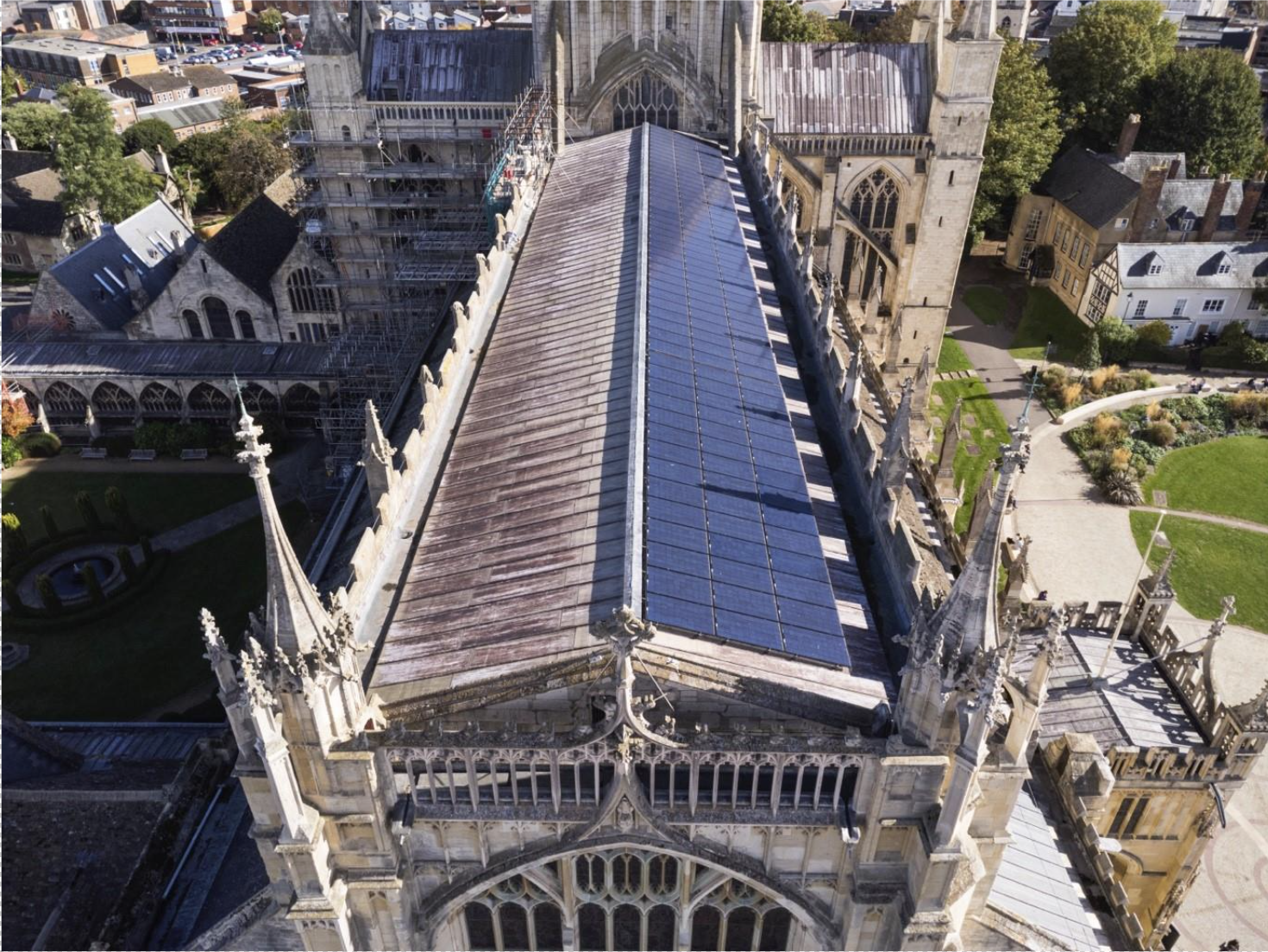 Alt text: An aerial photo looking down along the roof on a historic church. One side of the roof is covered by an array of solar panels.