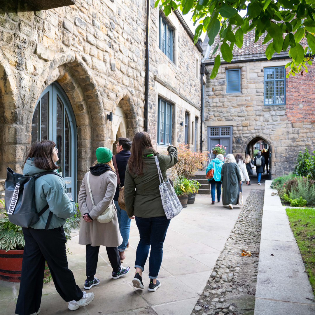 Photograph of a tour group walking through an historic building, they are looking at features and pointing them out to each other.