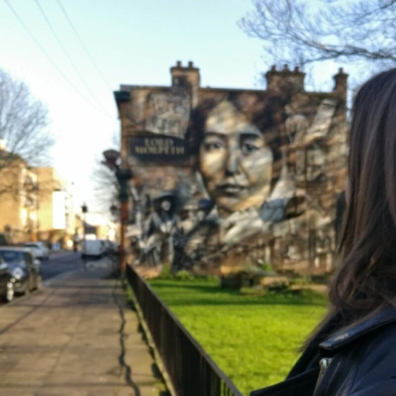 A woman is seen looking towards a mural of Sylvia Pankhurst on the side of a building in East London.