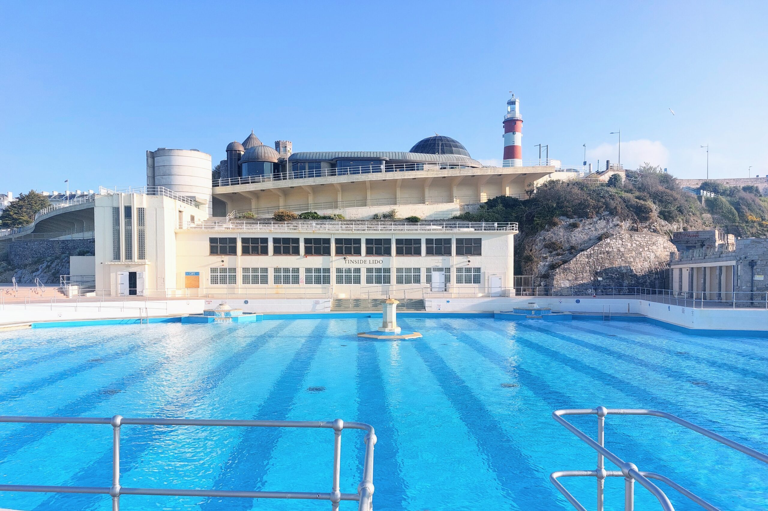 A photo of an outdoor or lido, a white building in the background and bright blue pool in the foreground