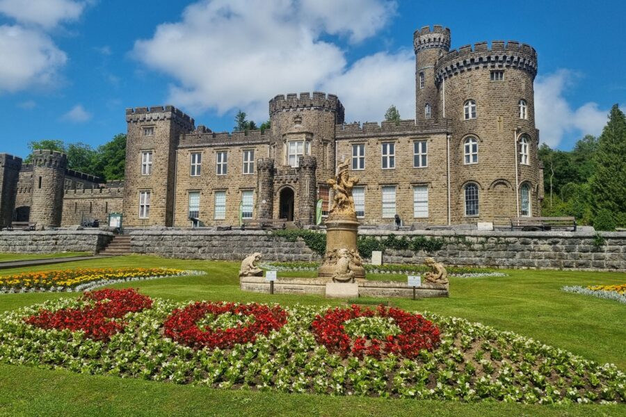 Cyfarthfa Castle with a blue sky. A flowerbed in the foreground with flowers in the shape of 200.