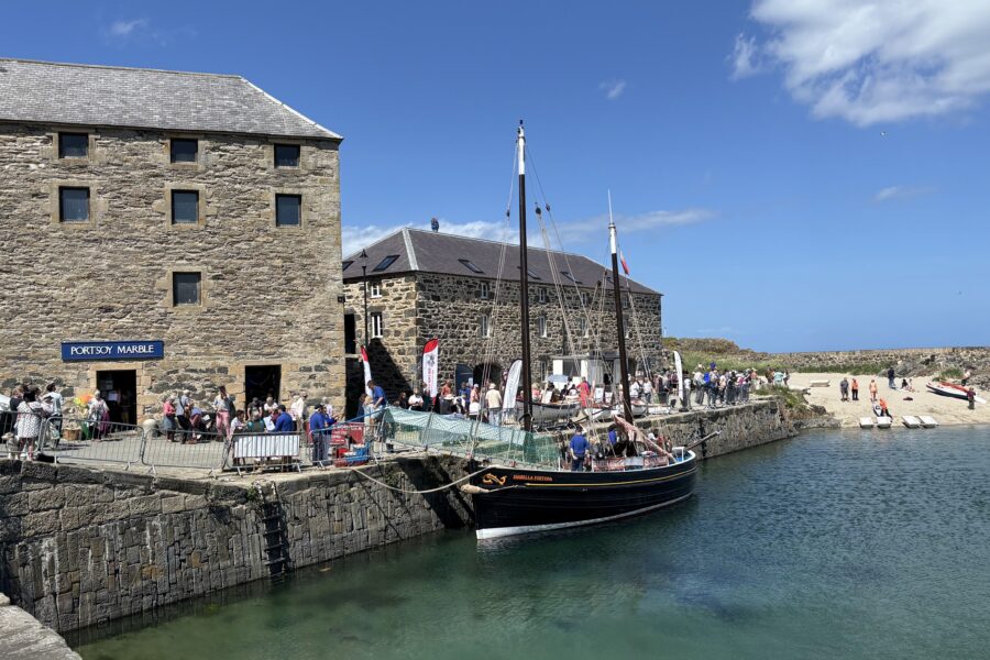 A photograph of Portsoy harbour, with a boat in the water and the Portsoy Marble Warehouse in the background.