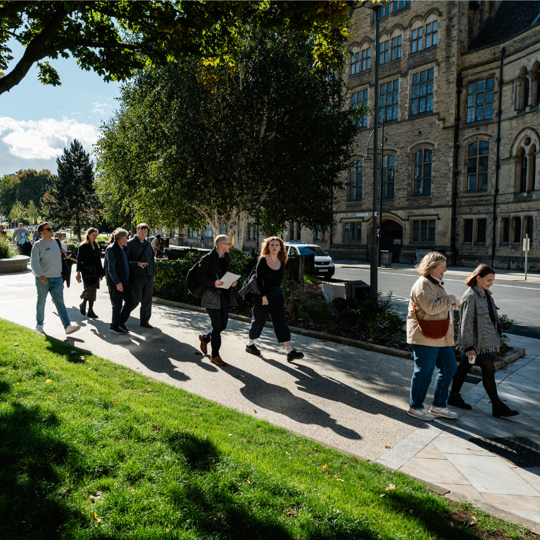 Photograph of a tour group walking through a green area with historic buildings in the background.