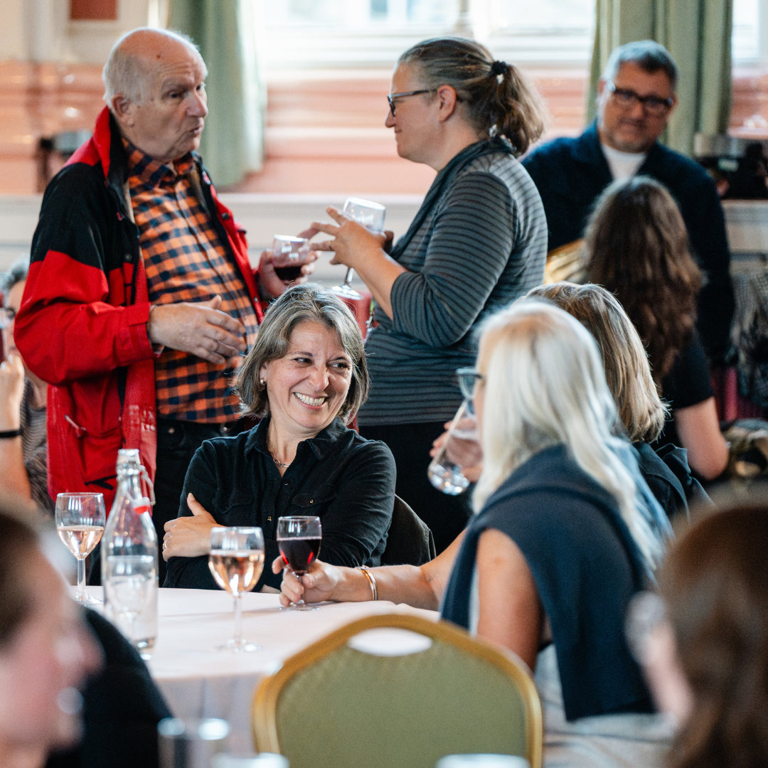 Photograph of groups of people at a drinks reception, they are talking and laughing
